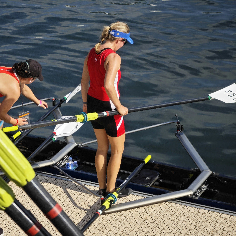 Rowers preparing to row on a boat with oars in the water.