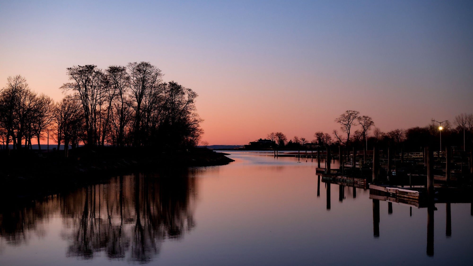 Evening scene at a lake with trees and dock, reflecting on water.