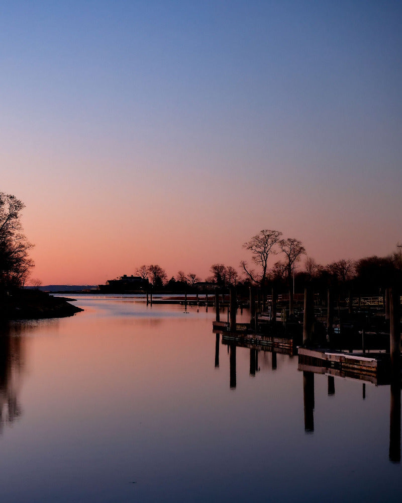 Evening scene at a lake with trees and dock, reflecting on water.